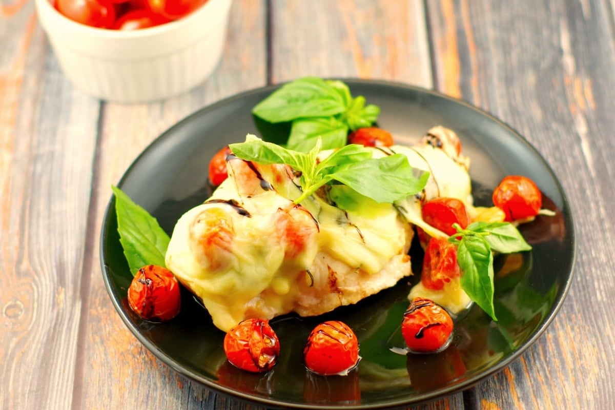 A piece of sheet pan chicken caprese on a black plate.