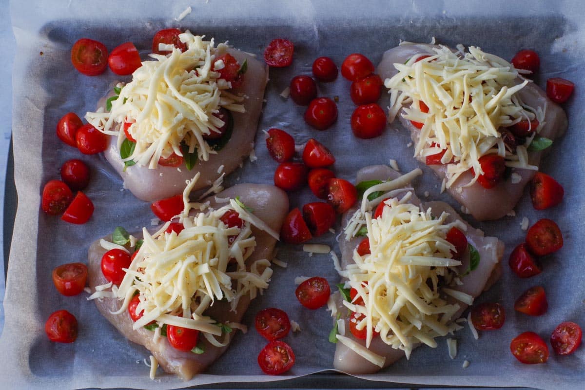 Shredded cheese added to tomato and basil on chicken breasts.