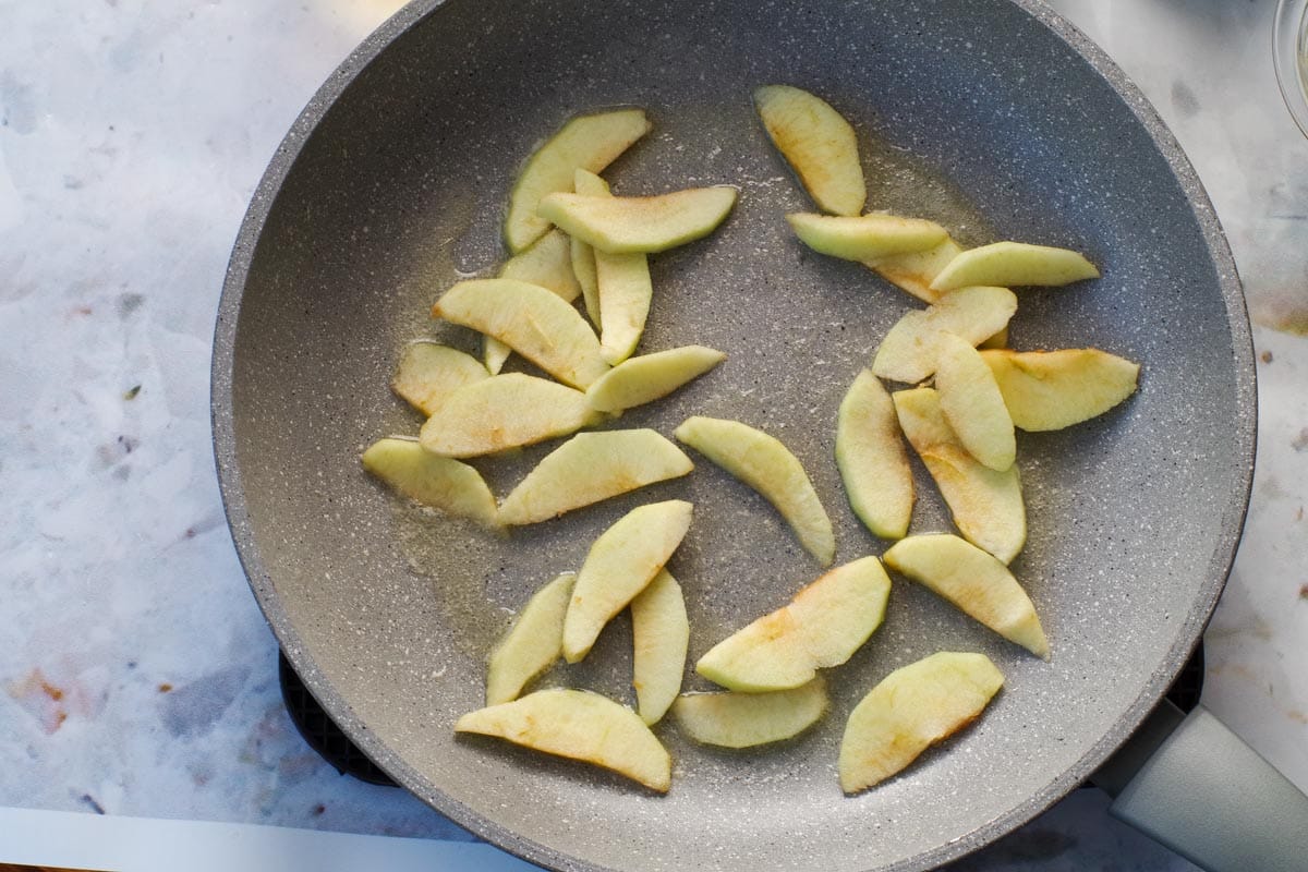 Apples cooking in butter in a frying pan.