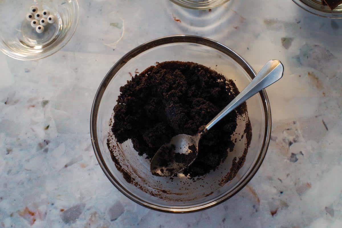 Chocolate crumbs and butter mixed together in glass bowl with spoon,