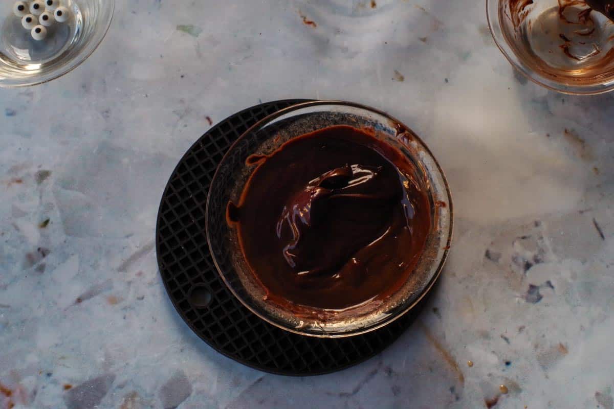 Melted chocolate in a glass bowl on a black trivet.