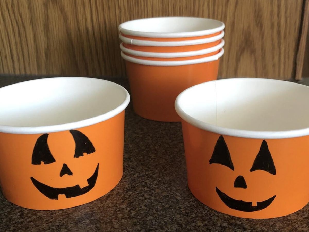 Orange dessert cups with jack o lantern faces drawn onto them.