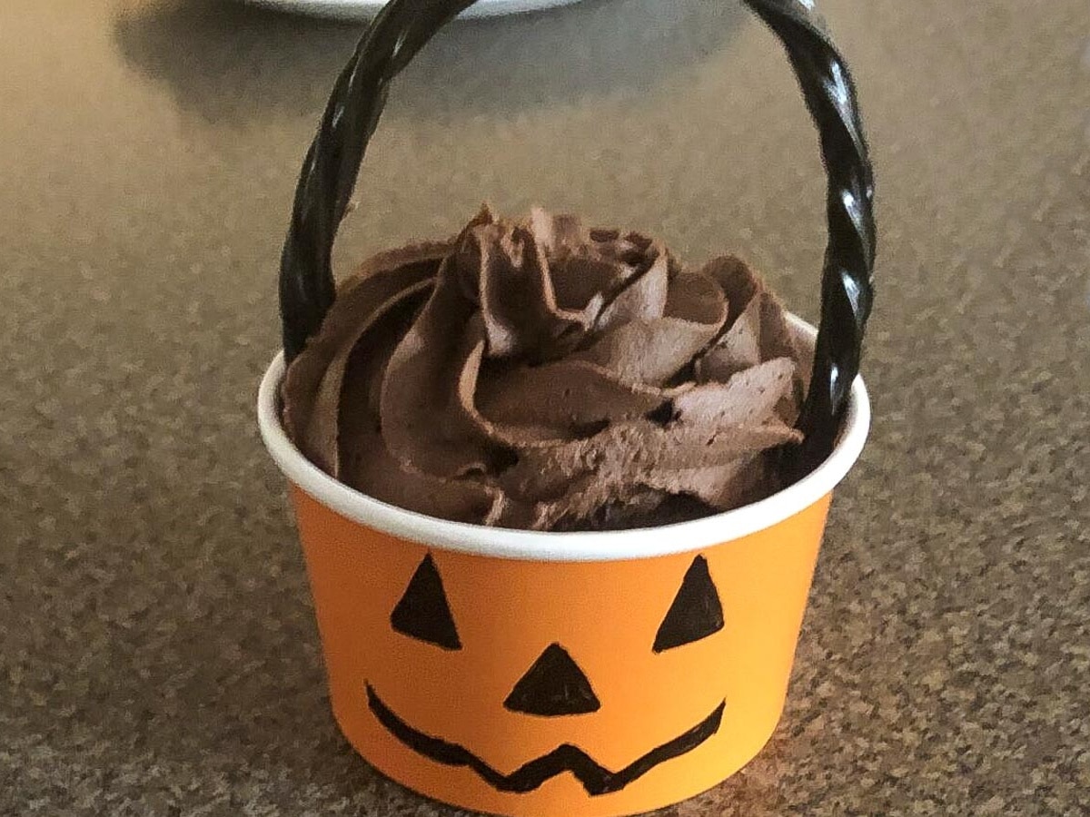 Cupcake placed inside orange jack o' lantern dessert cup with a licorice handle on top.