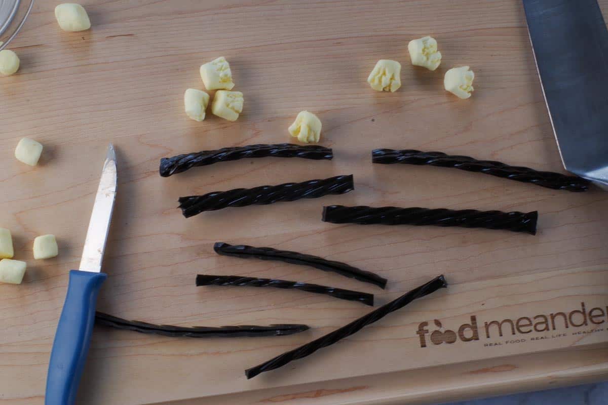 Licorice cut in half, then cut in half again, lengthwise, on a cutting board with cut marshallows.