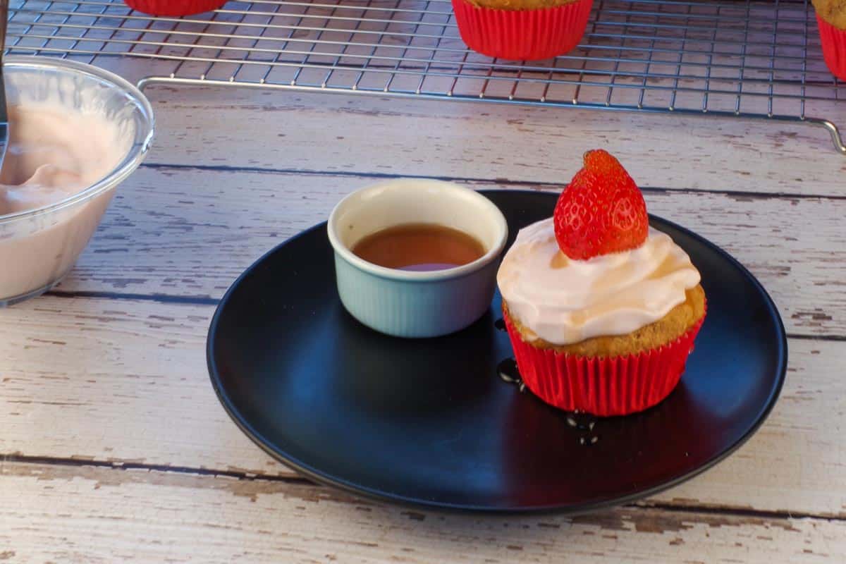 Strawberry Gingerbread Pancake Cupcake topped with Strawberry Greek yogurt, a strawberry and syrup with a little dish of syrup beside it.