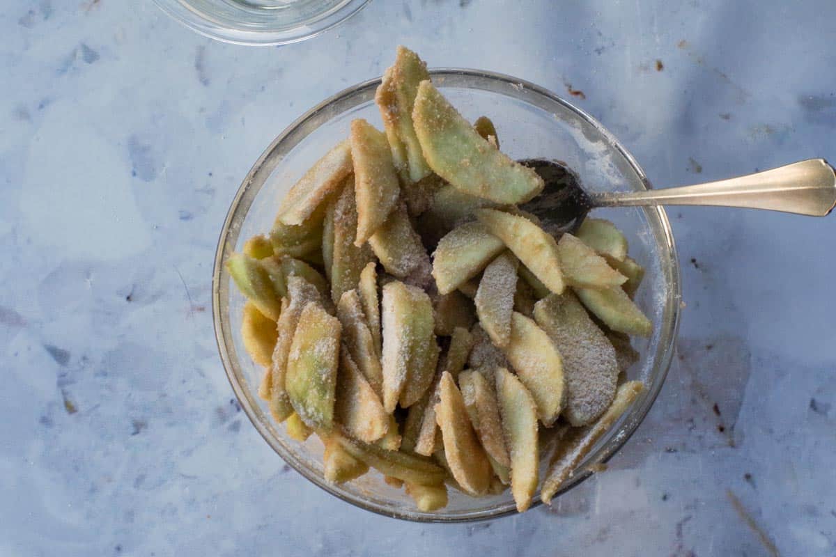 Sugar mixture mixed with the apples in a glass bowl, with spoon.
