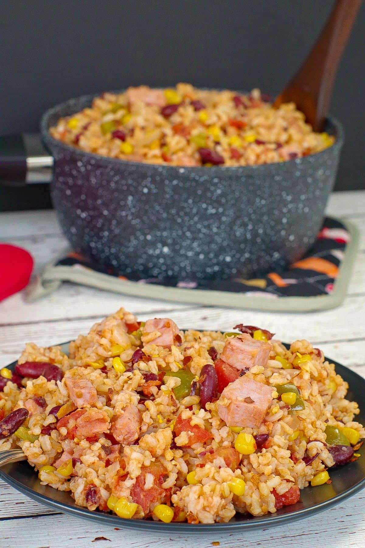 Ham rice and beans on a black plate with a pot of more in the background.