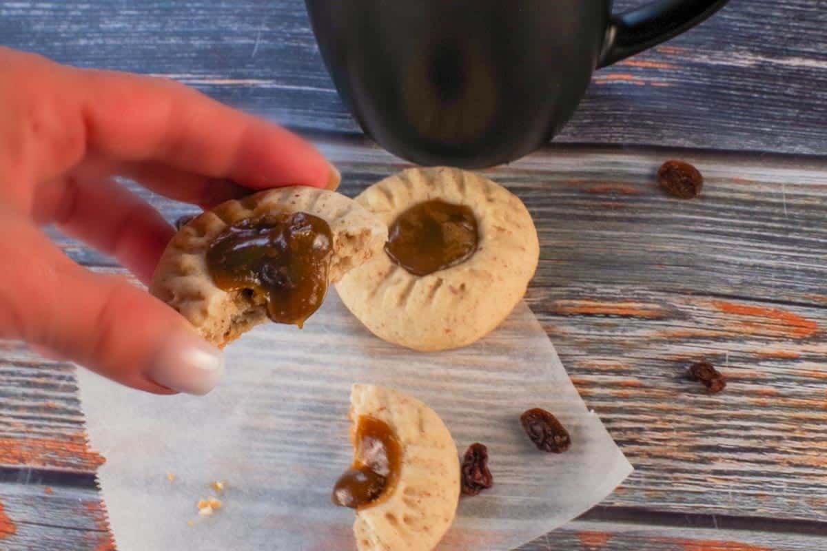 Butter tart cookies on parchment paper, with one split in half and being held up, with filling oozing out.