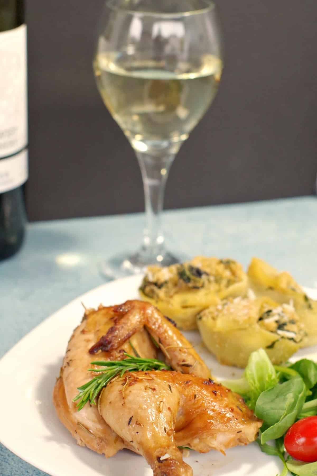 Half a Cornish Hen on a plate with pasta and salad and a glass of white wine in the background.