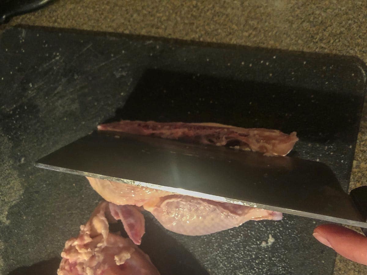 Cleaver being used to cut the backbone from one side of the Cornish Hen.