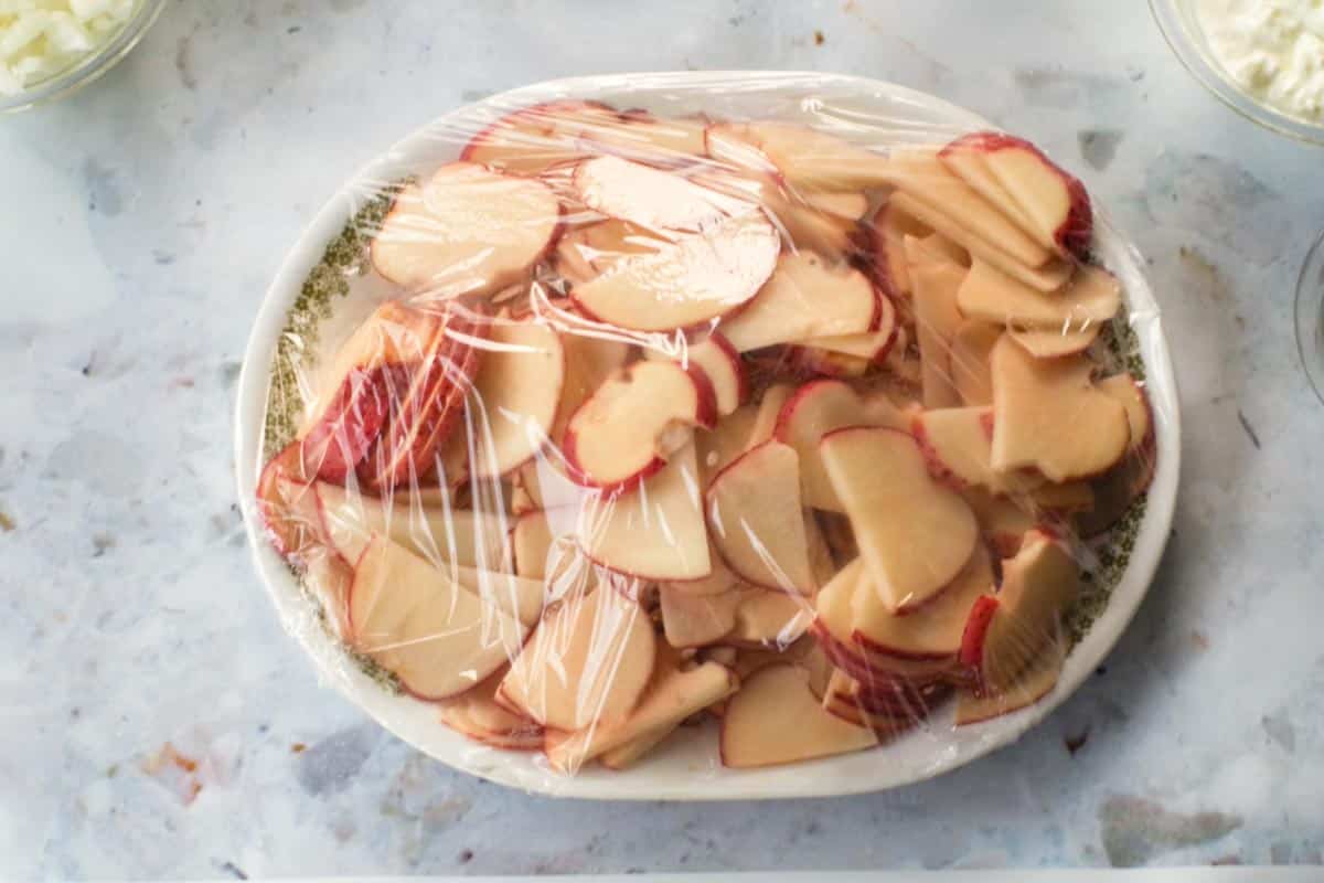 Sliced Potatoes on a platter covered with saran wrap.