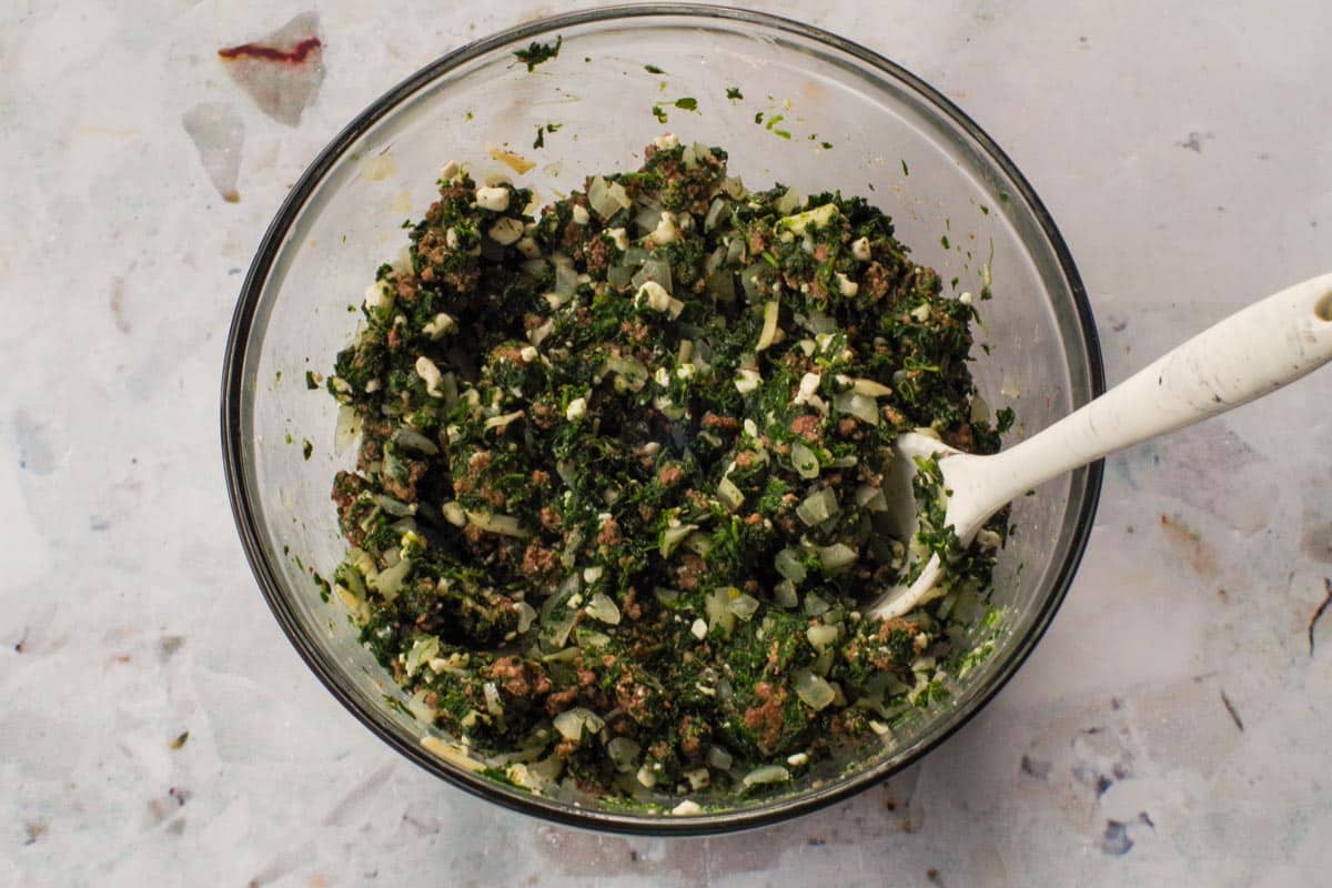 Cooked ground beef, spinach mixture in a glass bowl with silicone spoon.