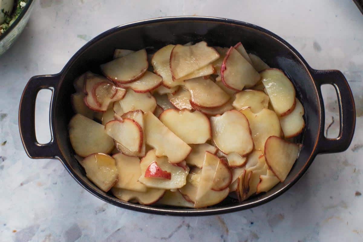 Half of the sliced potatoes in the bottom of the casserole dish, drizzled with half the butter.