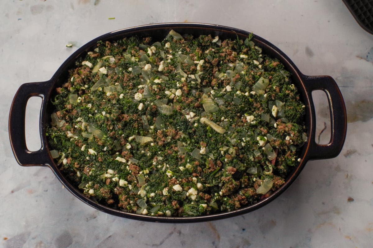 Spinach and beef mixture spread over the first layer of sliced potatoes and butter.