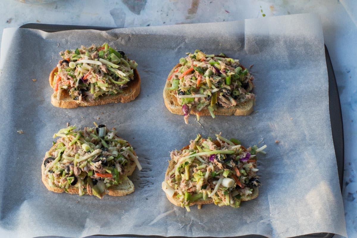 4 pieces of toast on a parchment covered baking sheet, topped with broccol slaw mixture.