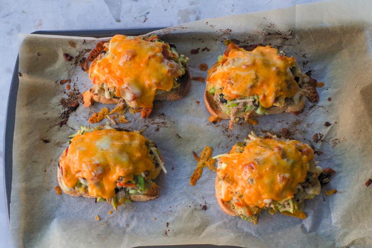 Cheese melted on tuna melts on parchment covered baking sheet.