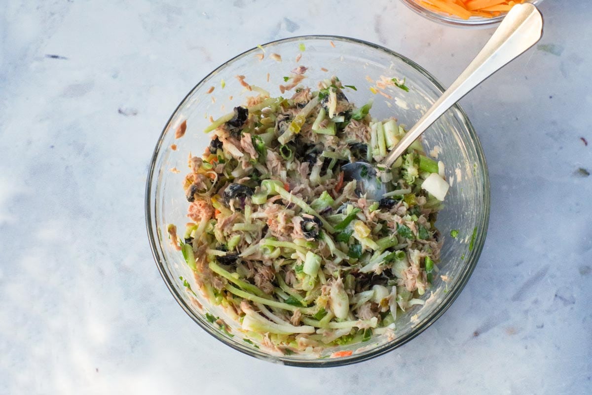 Mayonnaise mixture poured over broccoli mixture in glass bowl.