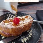 A Raspberry Stuffed French Toast Sandwich on a black plate with syrup being poured over it.