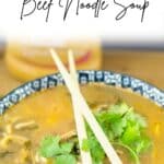 Asian Sesame Beef noodle soup with chopsticks resting on bowl and bottle of salad dressing in the background.