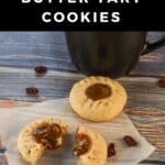 Butter tart cookies on parchment paper, with one split in half and filling oozing out. and black coffee mug in the background.