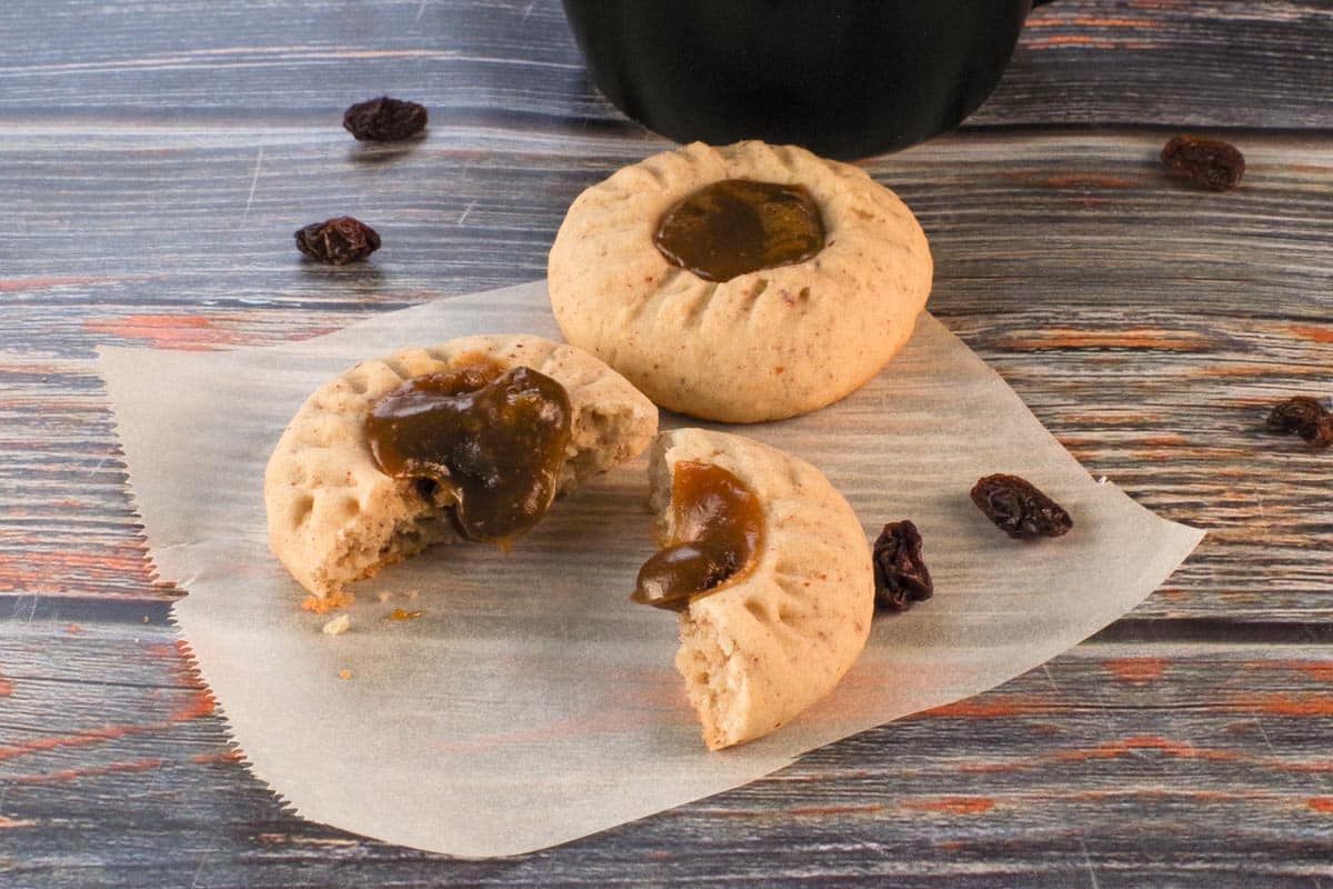 Butter tart cookies on parchment paper, with one split in half and filling oozing out.