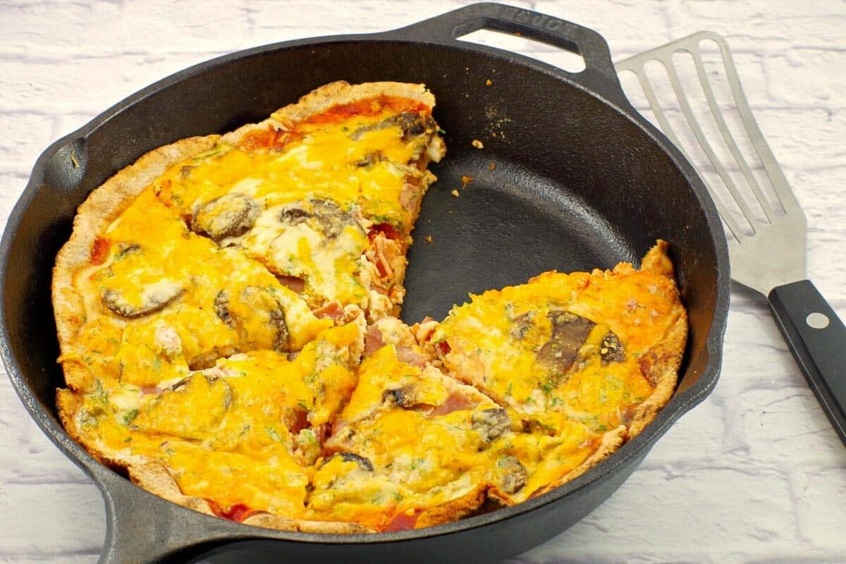 Healthy Breakfast pizza in a black cast iron pan with a piece missing (and turner beside the pan).