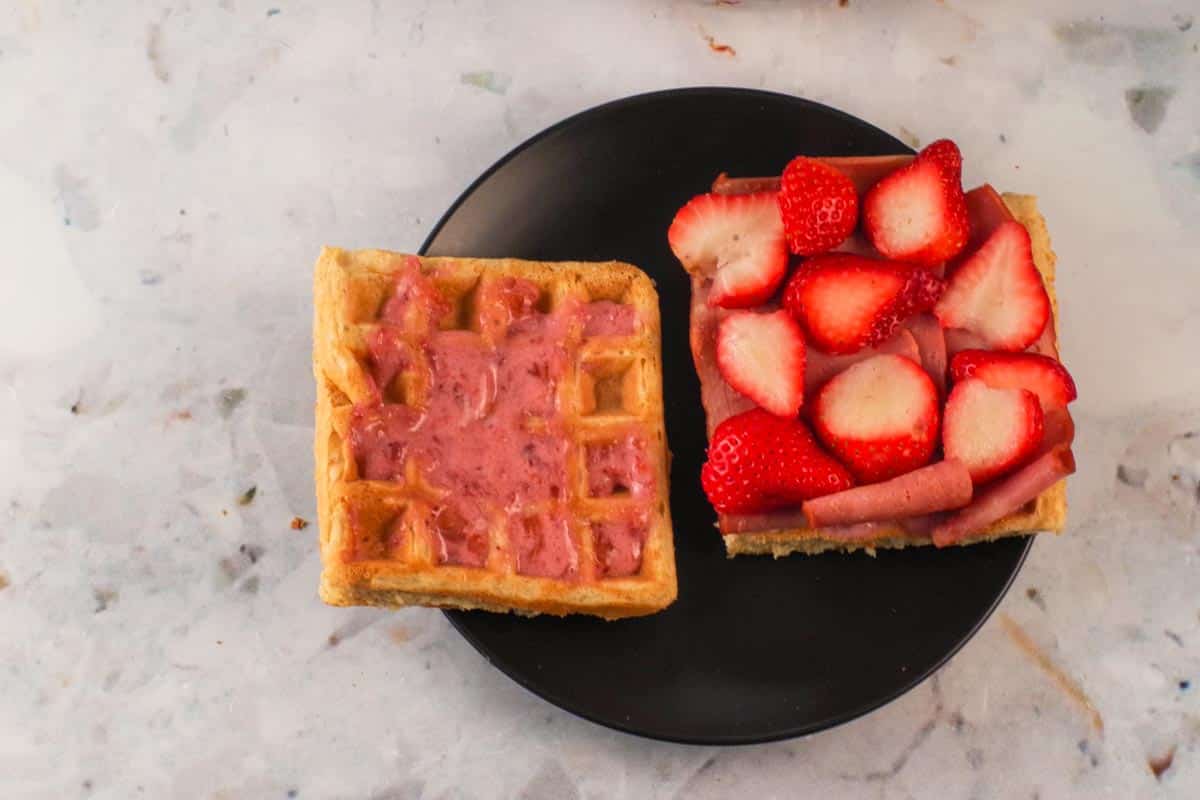 Sauce spread on one side of the waffles sandwich and chicken and berries on the other.