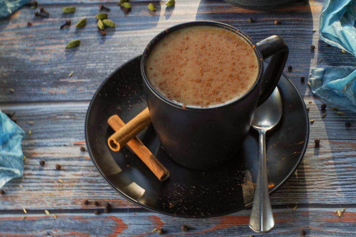 Homemade Masala Chai Tea in a black mug on a saucer with cinnamon sticks on the saucer.
