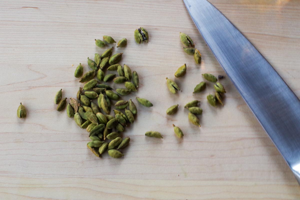 Cardamom seeds being split open with a chef's knife on a cutting board.