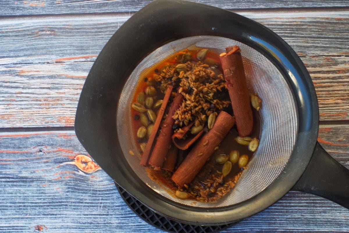 Tea bags and spices being strained through a fine mesh strainer.