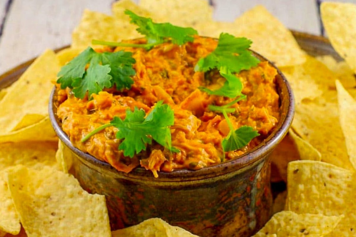 Hot Artichoke Pizza Dip in a bowl with tortilla chips around it on a platter.