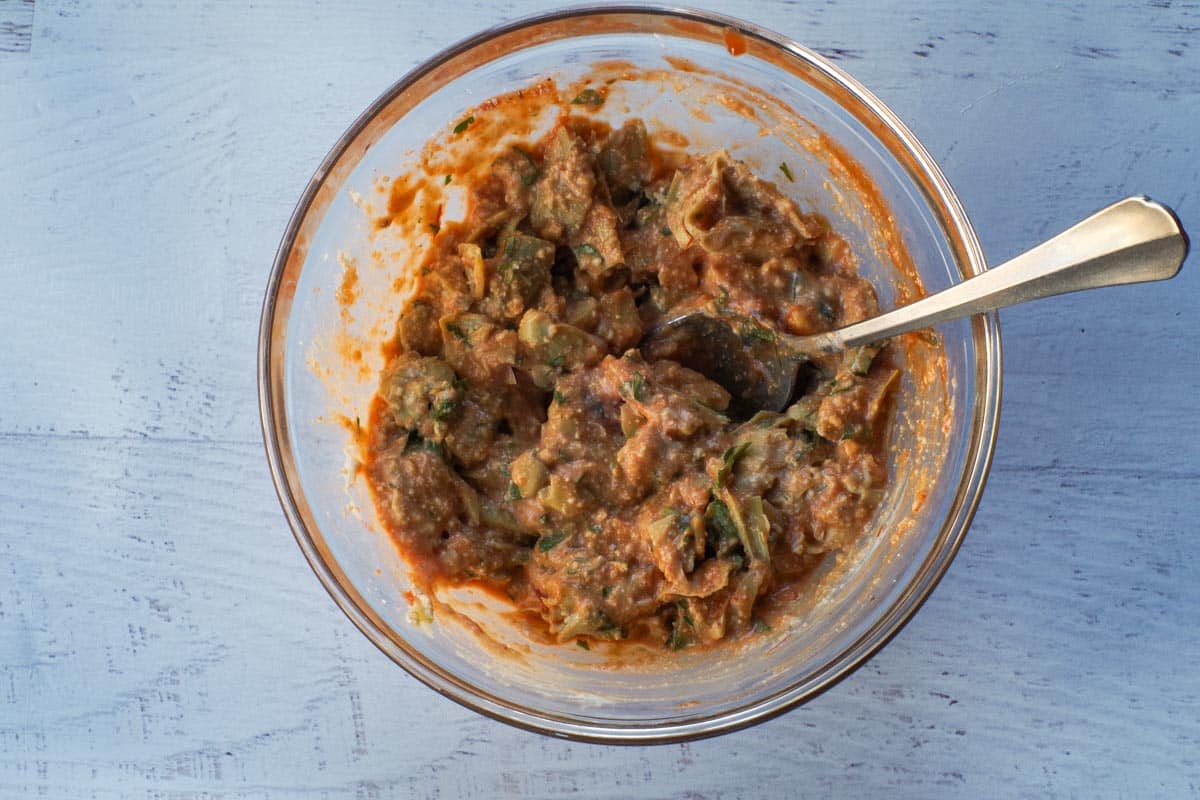 Baked Artichoke Dip ingredients mixed together in a glass bowl, with a spoon.