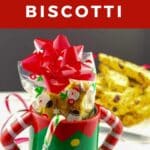 Holiday Biscotti packaged and placed in an elf mug with more Christmas biscotti in a cookie tin in the background.