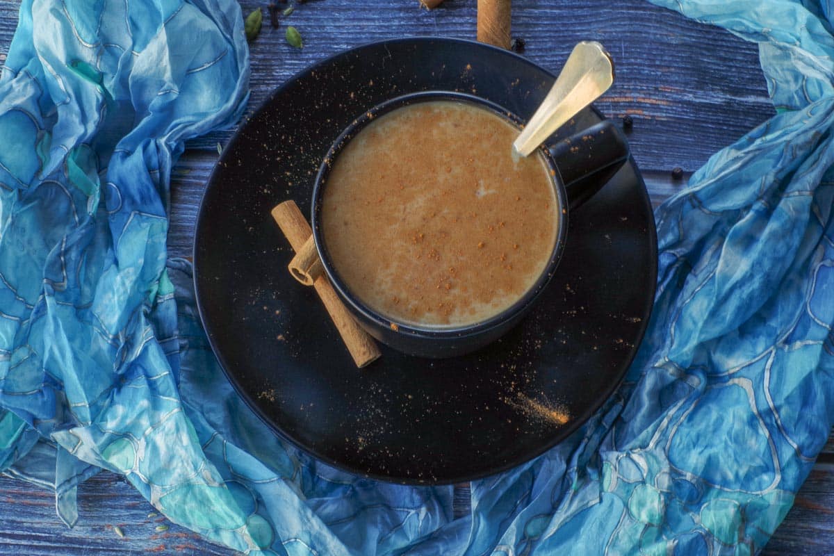 Masala Chai Tea in a black mug with a spoon in it and a blue scarf encircling it.