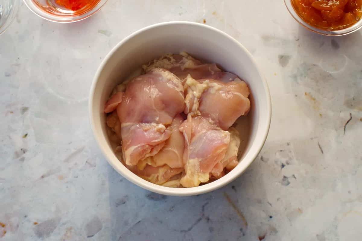 Raw chicken thigh pieces in small white casserole dish.