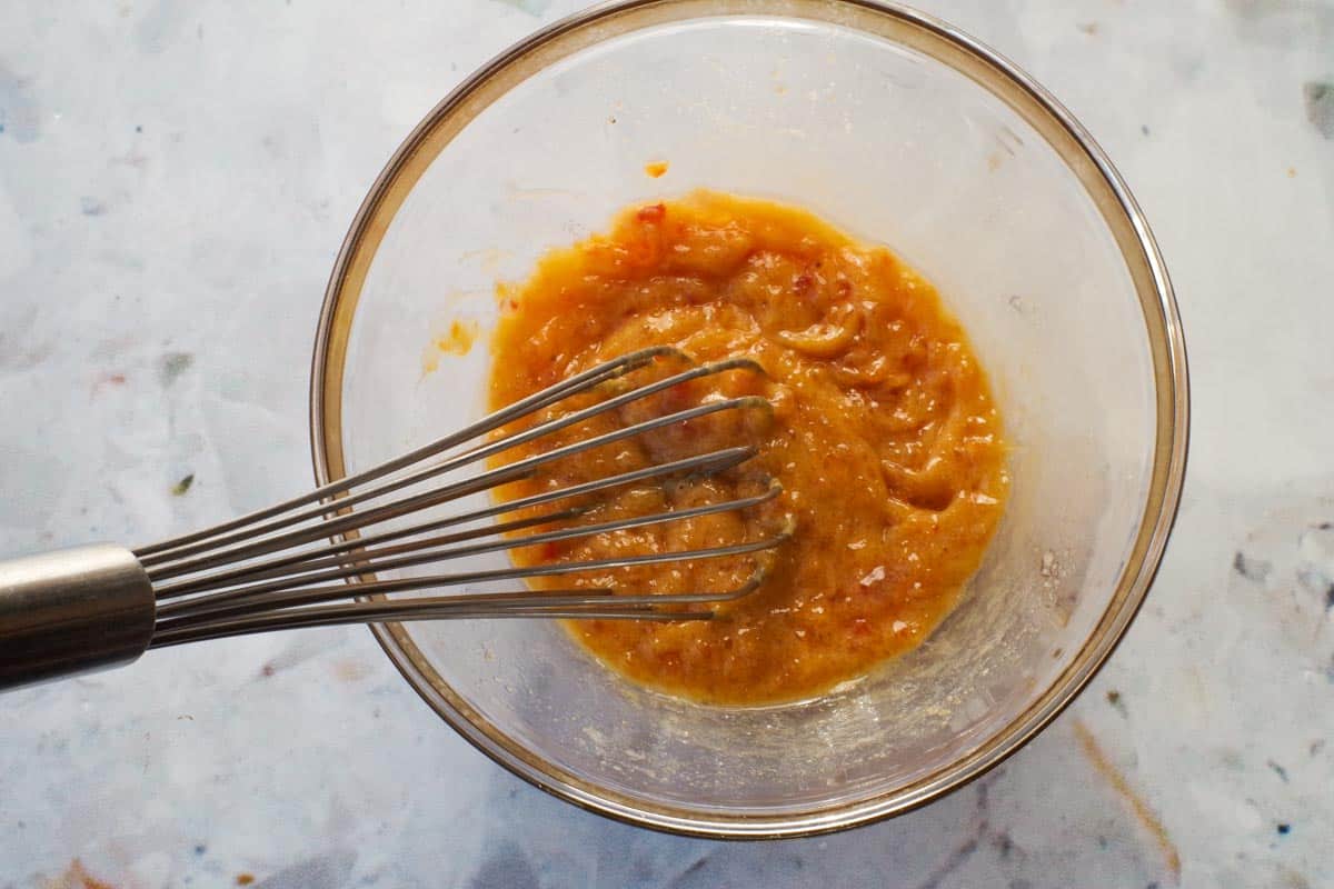 Apricot sauce mixed together in a glass bowl with whisk.