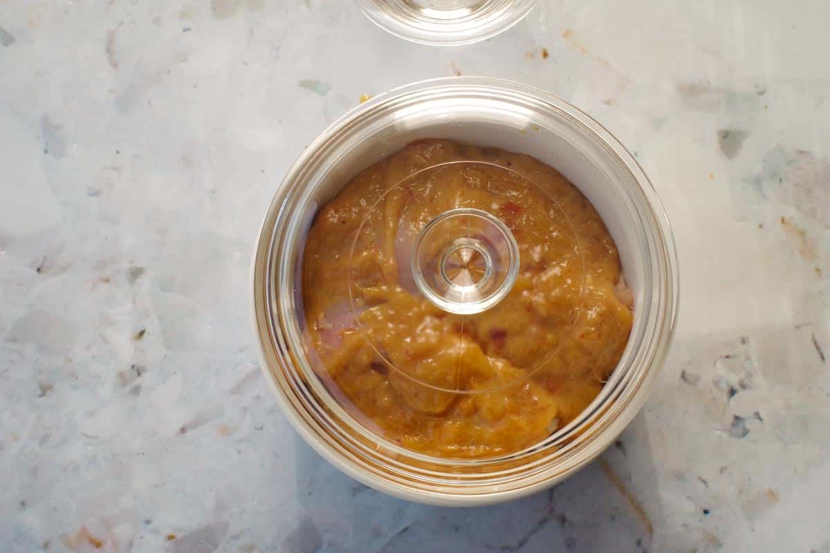 Small white casserole dish with chicken in it, covered with glass lid.
