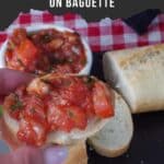 Bruschetta on Baguette being held up over more bruscheetta and baguette on a black tray.