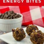 3 Chocolate Cherry energy bites on a white plate with a dish of chocolate chips in the background.
