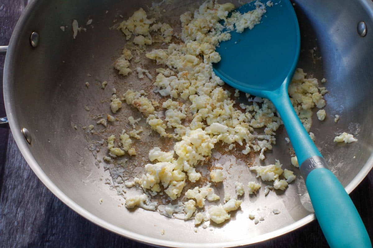 Cooked egg in wok with a blue spatula.