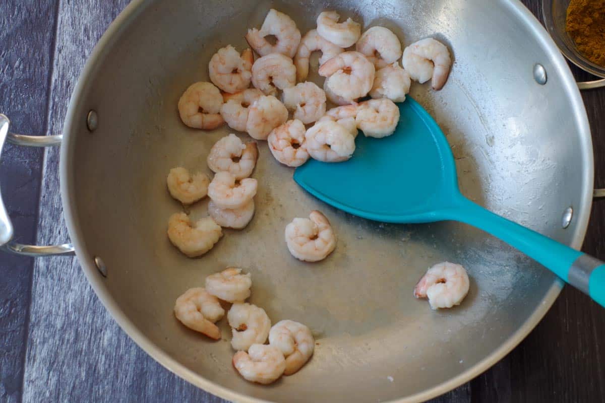Shrimp being cooked in wok with blue spatula.