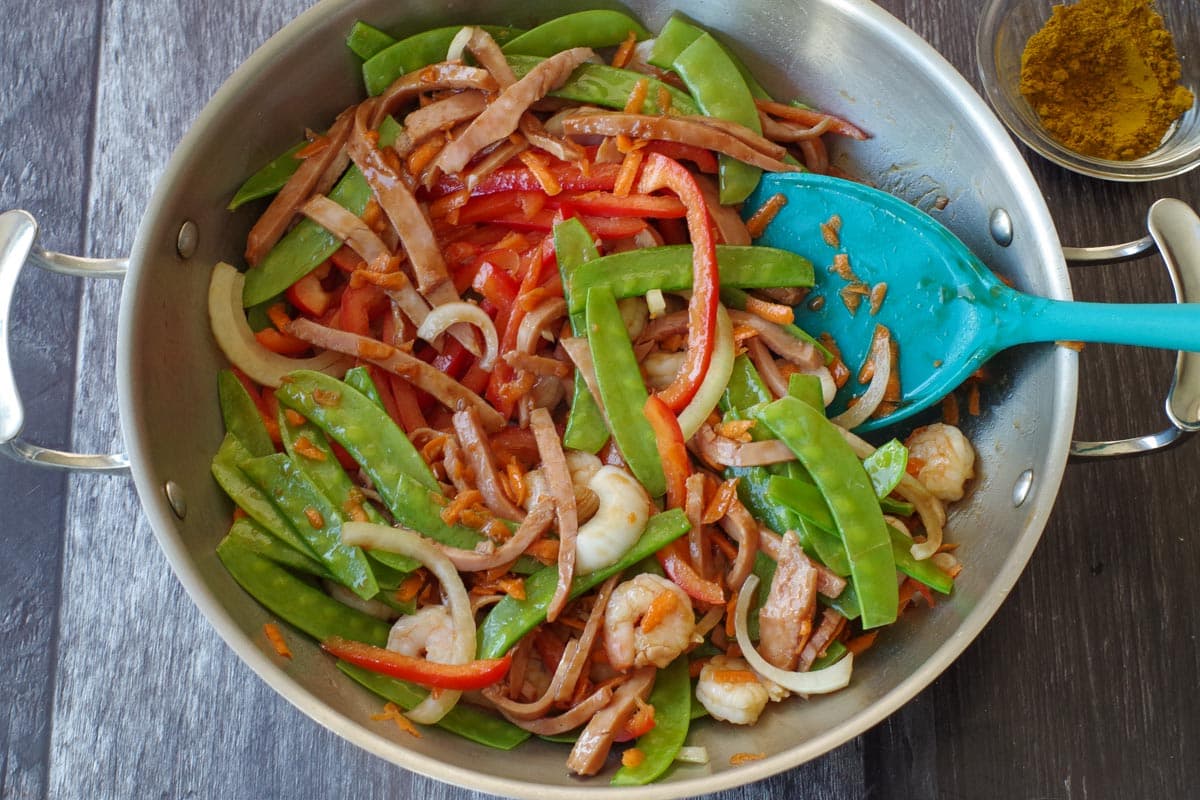 Ham and vegetables added to the wok, with blue spatula.