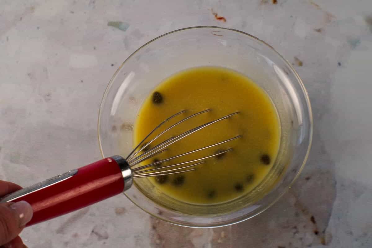 Mustard, capers and chicken broth in a glass bowl being whisked together.
