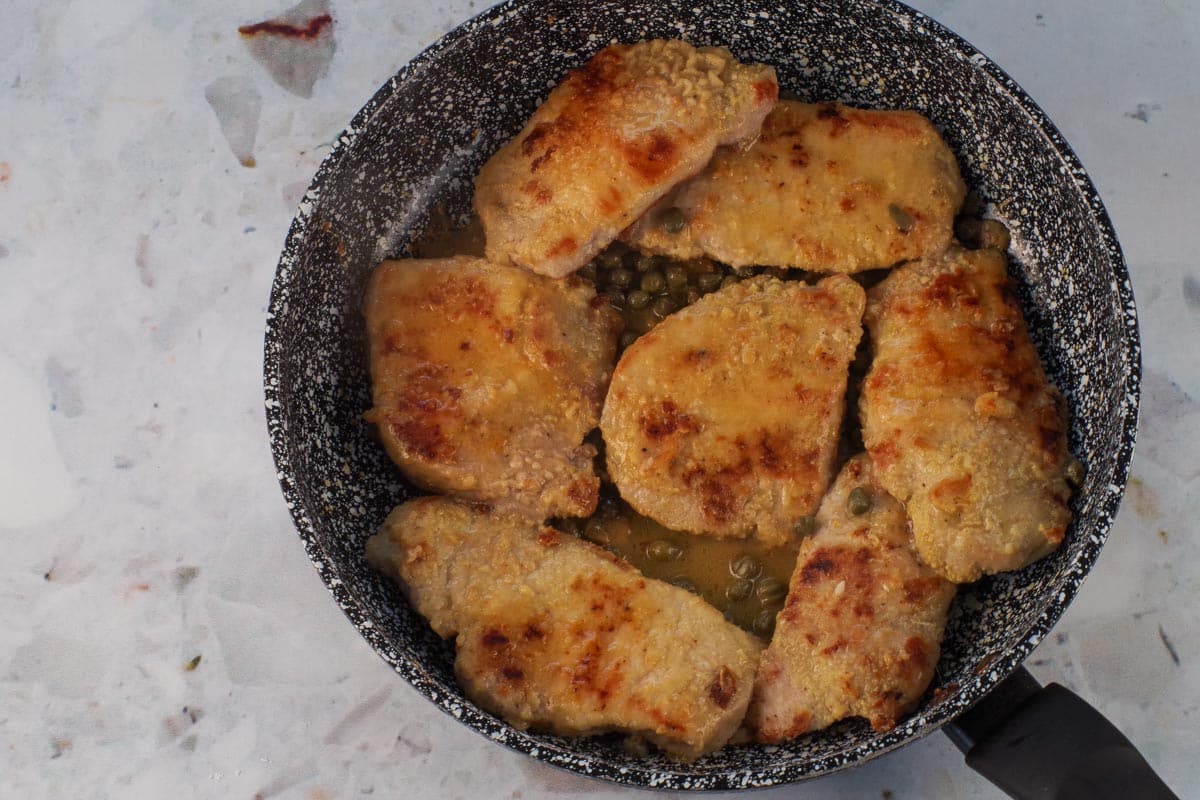 Pork cooked in broth and capers in a frying pan.