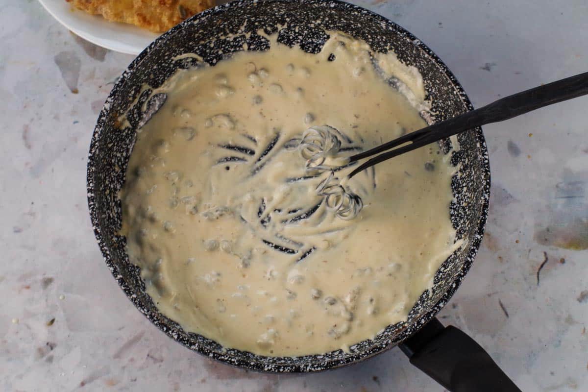Yogurt being whisked into sauce in the pan.