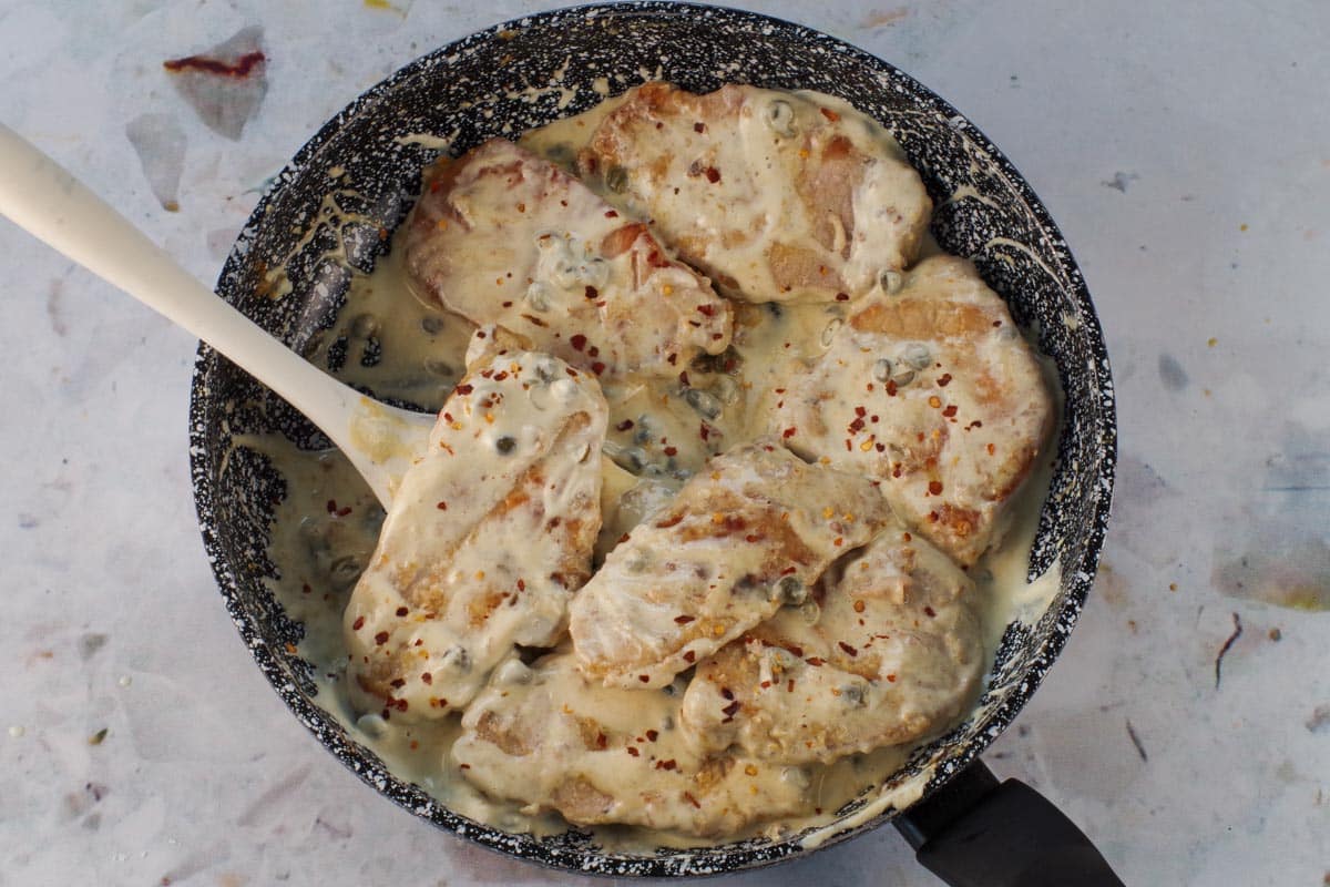 Pork added back into the sauce in the pan with spoon.