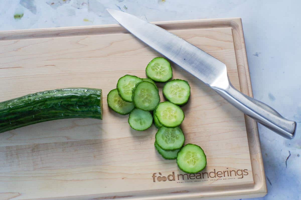 Cucumber cut into rounds on a wooden cutting board with a sharp knife.