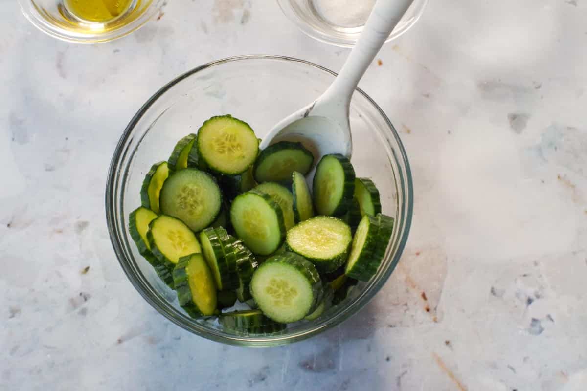 Sliced cucumber with salt in a glass bowl with a spoon,