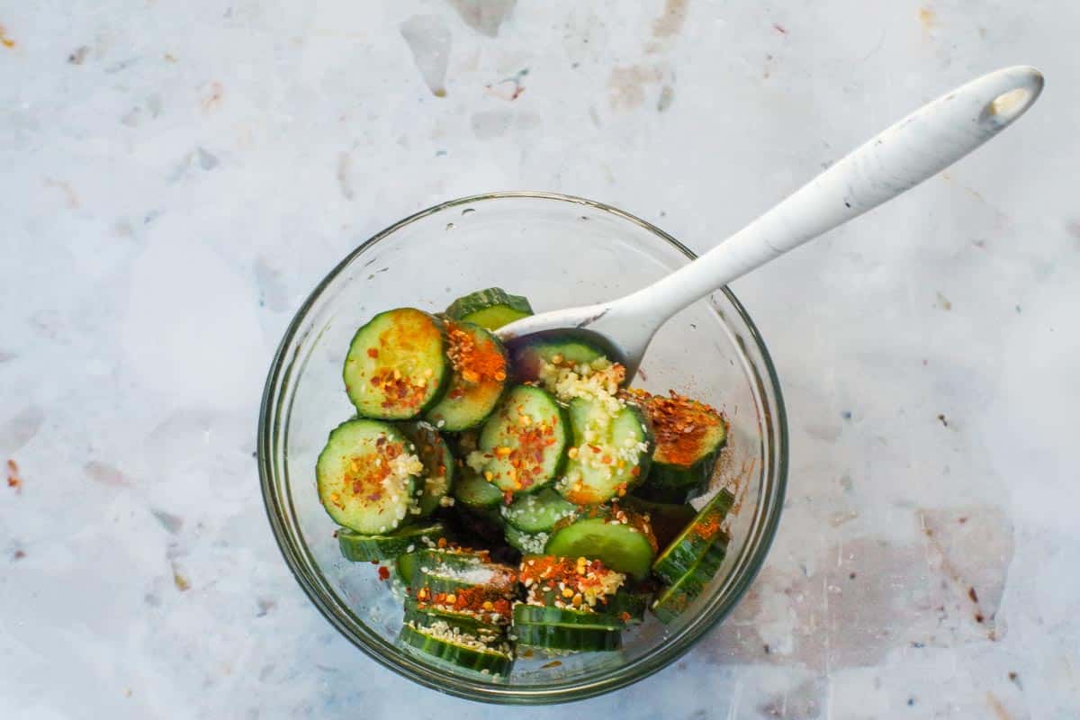 Remaining ingredients added to cucumbers and salt in glass bowl with silicone spoon.