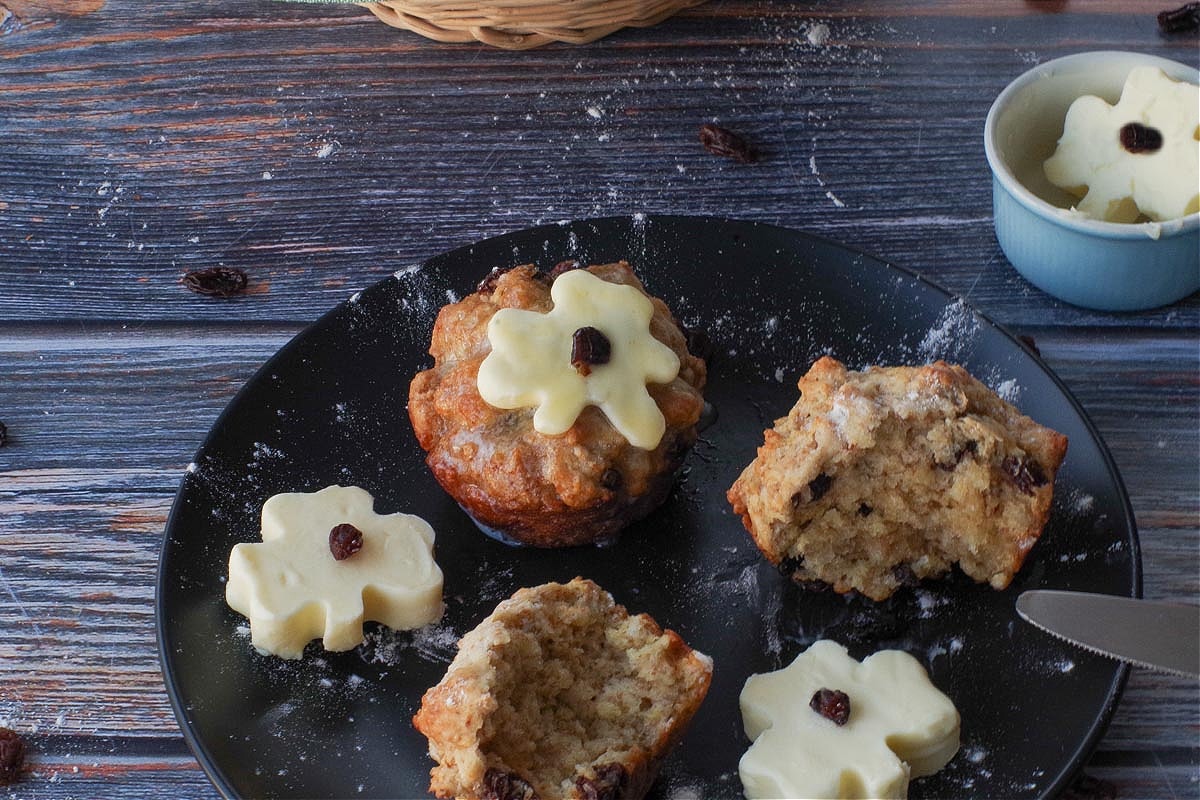 Two Healthy Irish Soda Bread Muffins on a black plate with shamrock butter with one shamrock butter melting on top of one of the muffins.